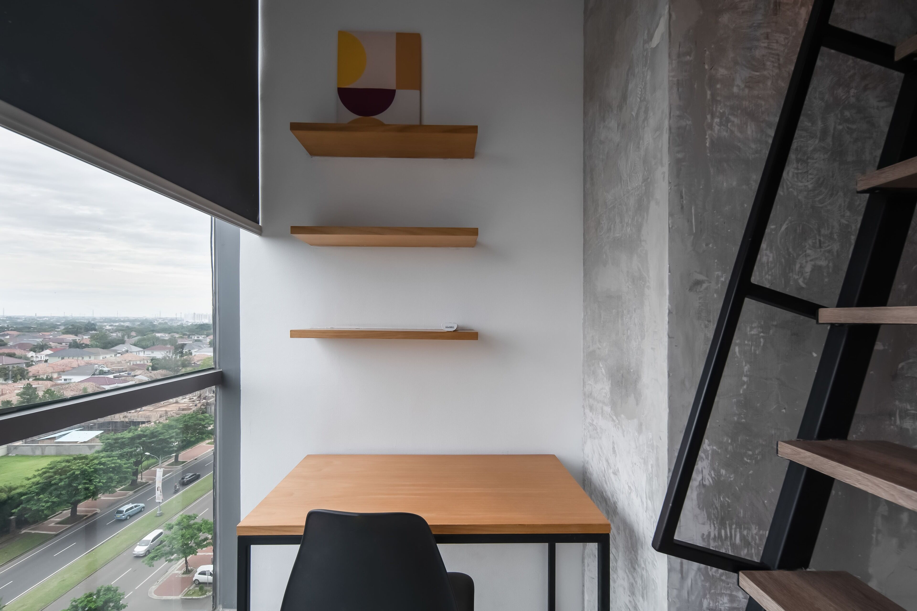 A modern room with a wooden desk, black chair, and three wooden shelves against a white wall.