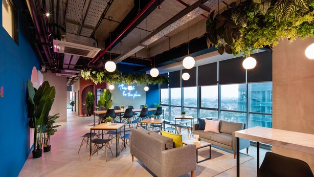 A modern office space with a high ceiling, exposed pipes, and large windows offering a city view. - Cove Hillcrest (Curug)