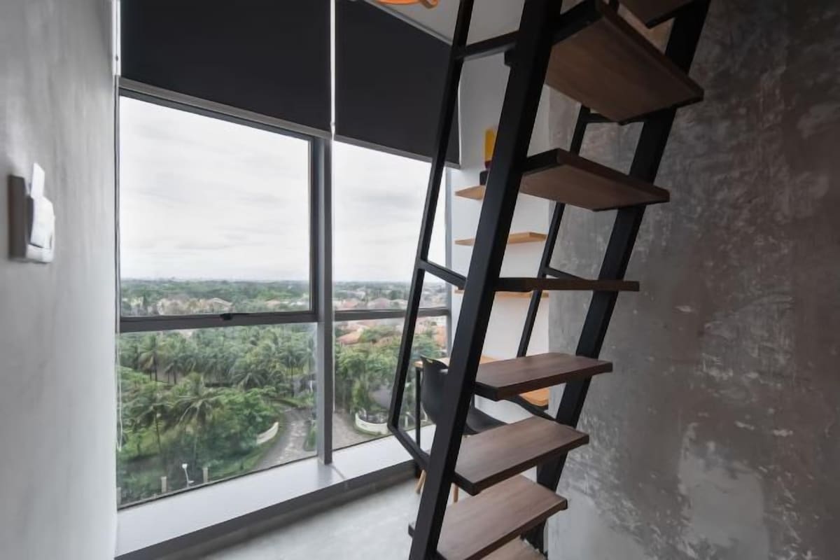 Ein Zimmer mit großem Fenster, einer schwarzen Metallleiter und Blick auf Grün.