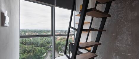 A room with a large window, a wooden ladder, and a view of a cityscape and greenery.