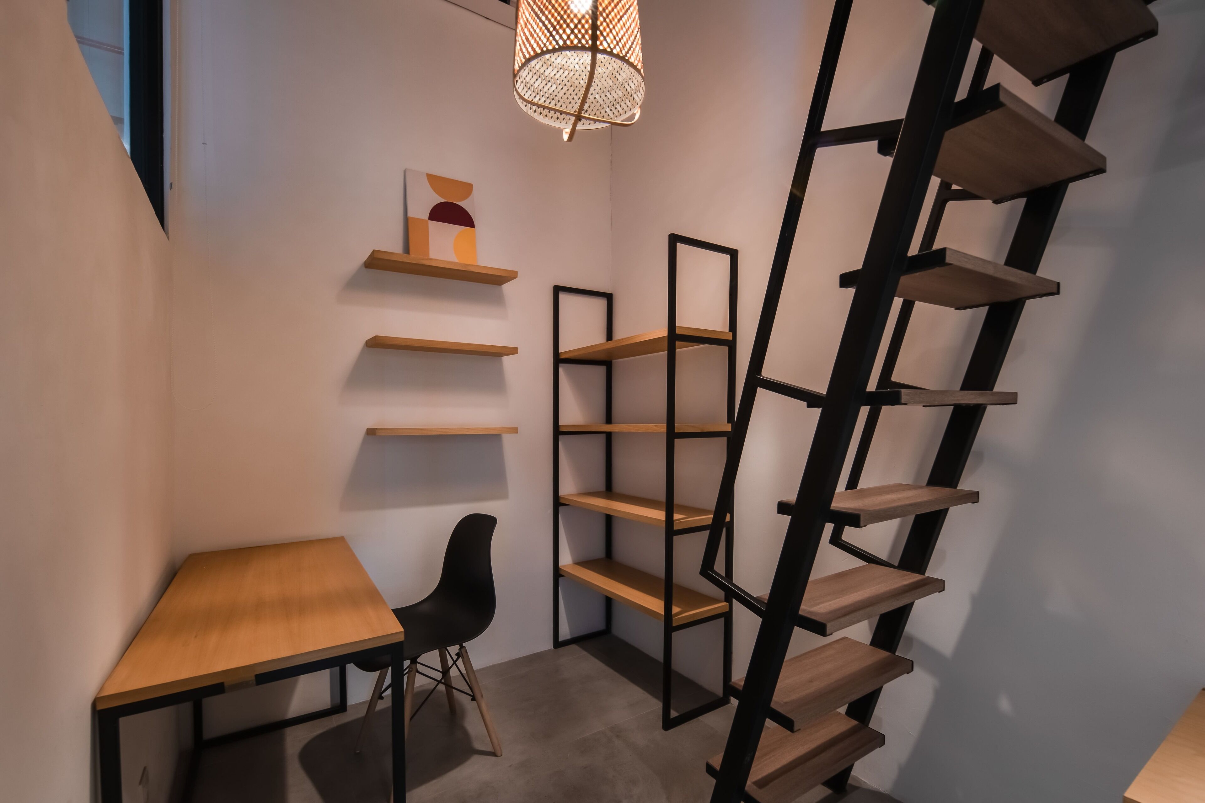 A corner room with a wooden desk, black chair, and multiple shelves.