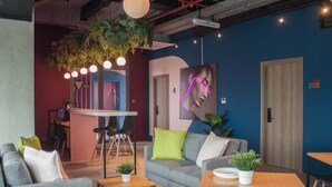 A modern lounge area with a grey sofa, a wooden table, and a bar area in the background. - Cove Hillcrest (Curug)
