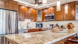 A modern kitchen with wooden cabinets, stainless steel appliances, and a large marble island. - Stunning Deluxe Ocean View W/Lanai-Kamaole Sands (Kihei)