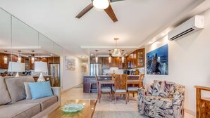 A modern living room with a sofa, coffee table, and patterned armchair. A dining area with a table and chairs is visible in the background. - Stunning Deluxe Ocean View W/Lanai-Kamaole Sands (Kihei)