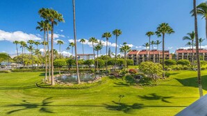A well-manicured golf course with palm trees, a pond, and a hotel in the background. - Stunning Deluxe Ocean View W/Lanai-Kamaole Sands (Kihei)