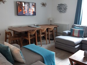 Una sala de estar moderna con una mesa de comedor de madera, un sofá gris y un televisor montado en la pared.