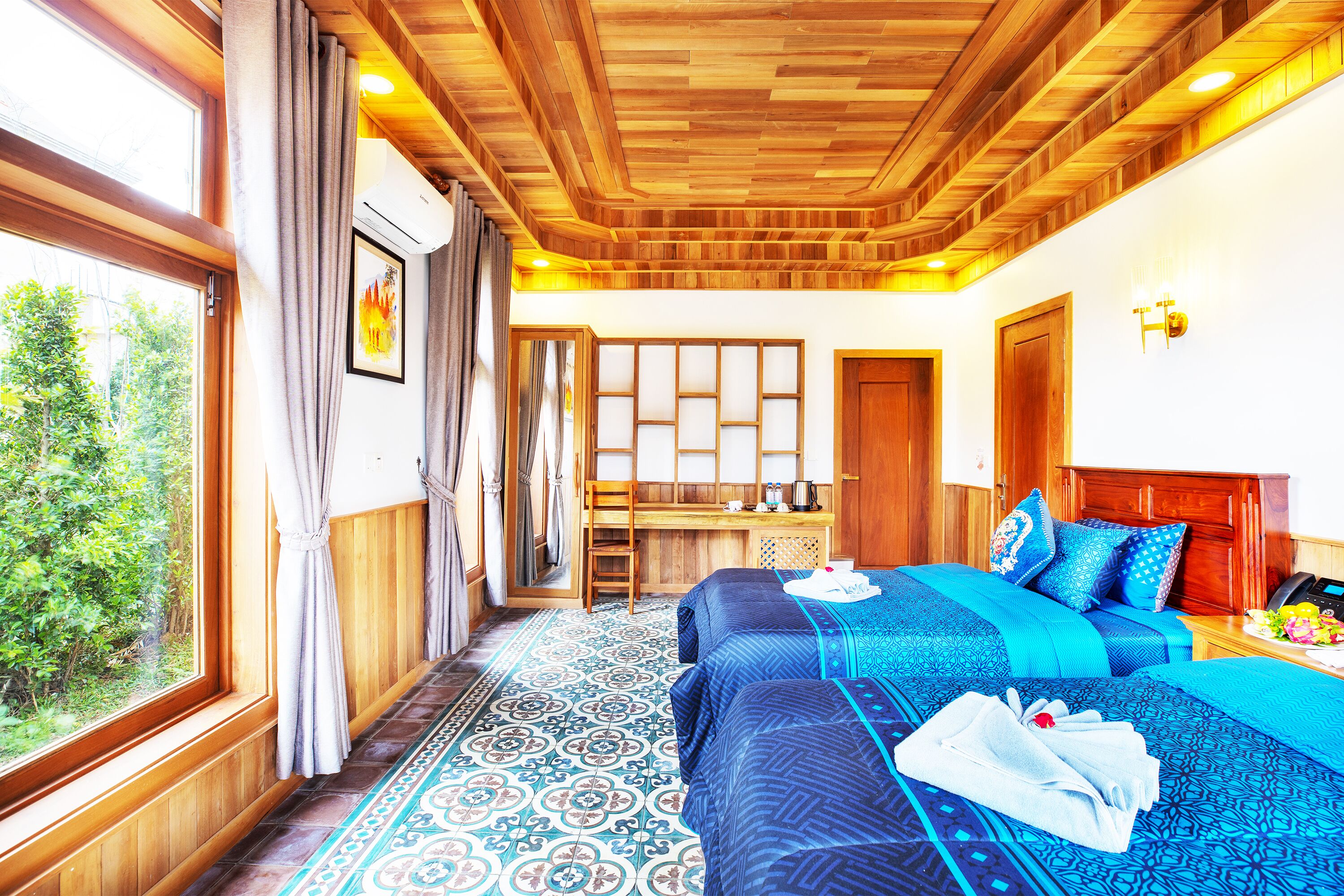 Habitación de hotel con dos camas, techo de madera, vista a zonas verdes y una pequeña cocina.