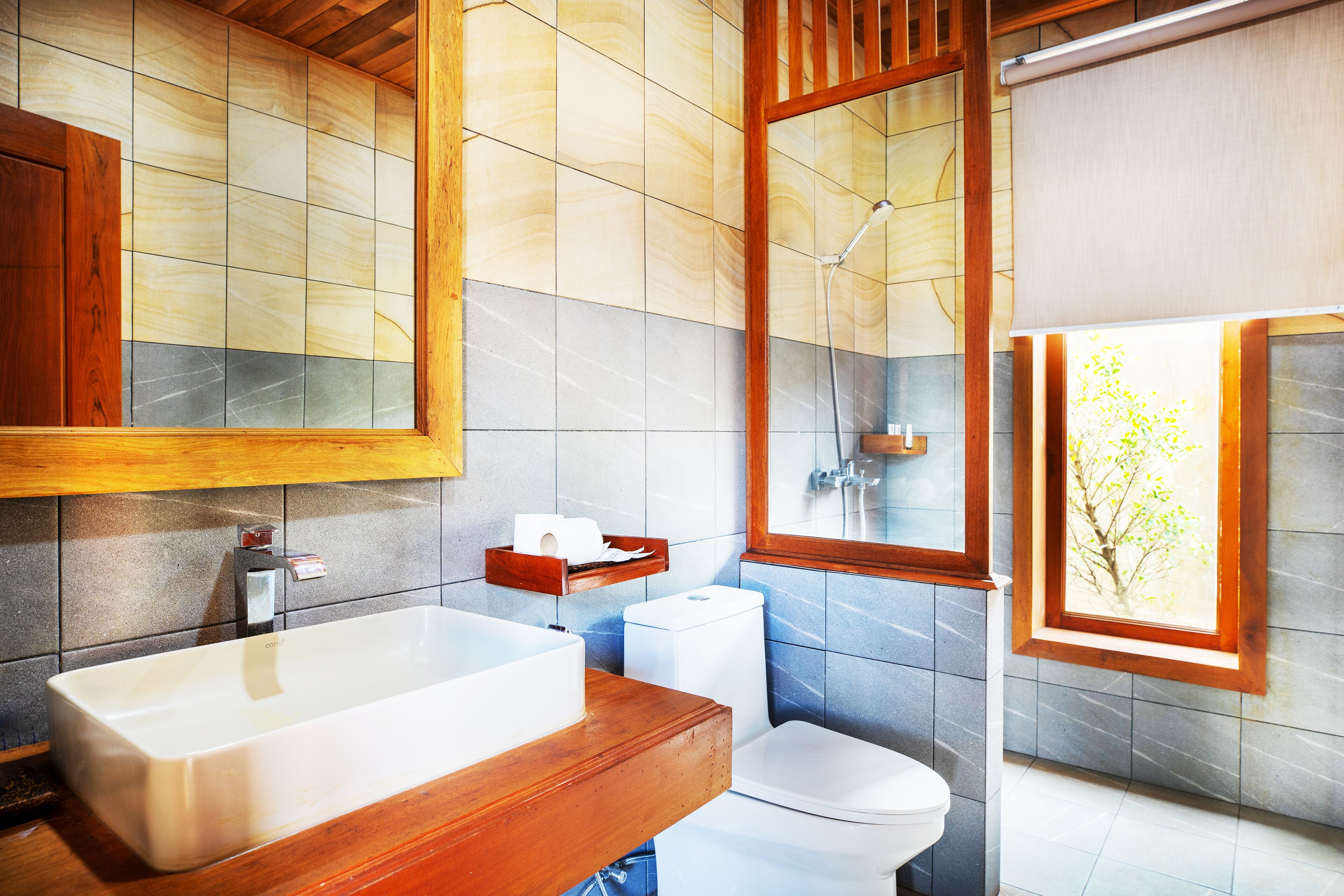 Een moderne badkamer met een houten wastafel, een grote spiegel, een douche en een raam met uitzicht op bomen.