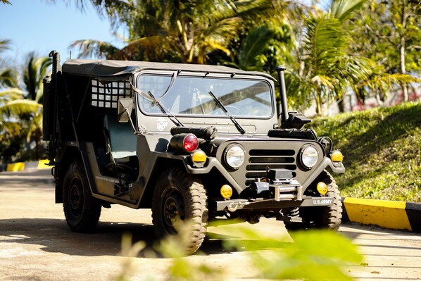 A U.S. Army vehicle with a cargo bed, driving on a road with palm trees in the background. - KNN Resort Mondulkiri (Sen Monorom)