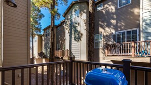 A deck with a barbecue grill, wooden railings, and a view of a multi-story building with windows and a balcony. - Luxurious AC Home Near Heart of Downtown, NAU, Snowbowl, Historic Route 66 (Flagstaff)