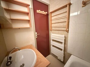 Une salle de bain avec un lavabo blanc, une porte rouge et un porte-serviettes.