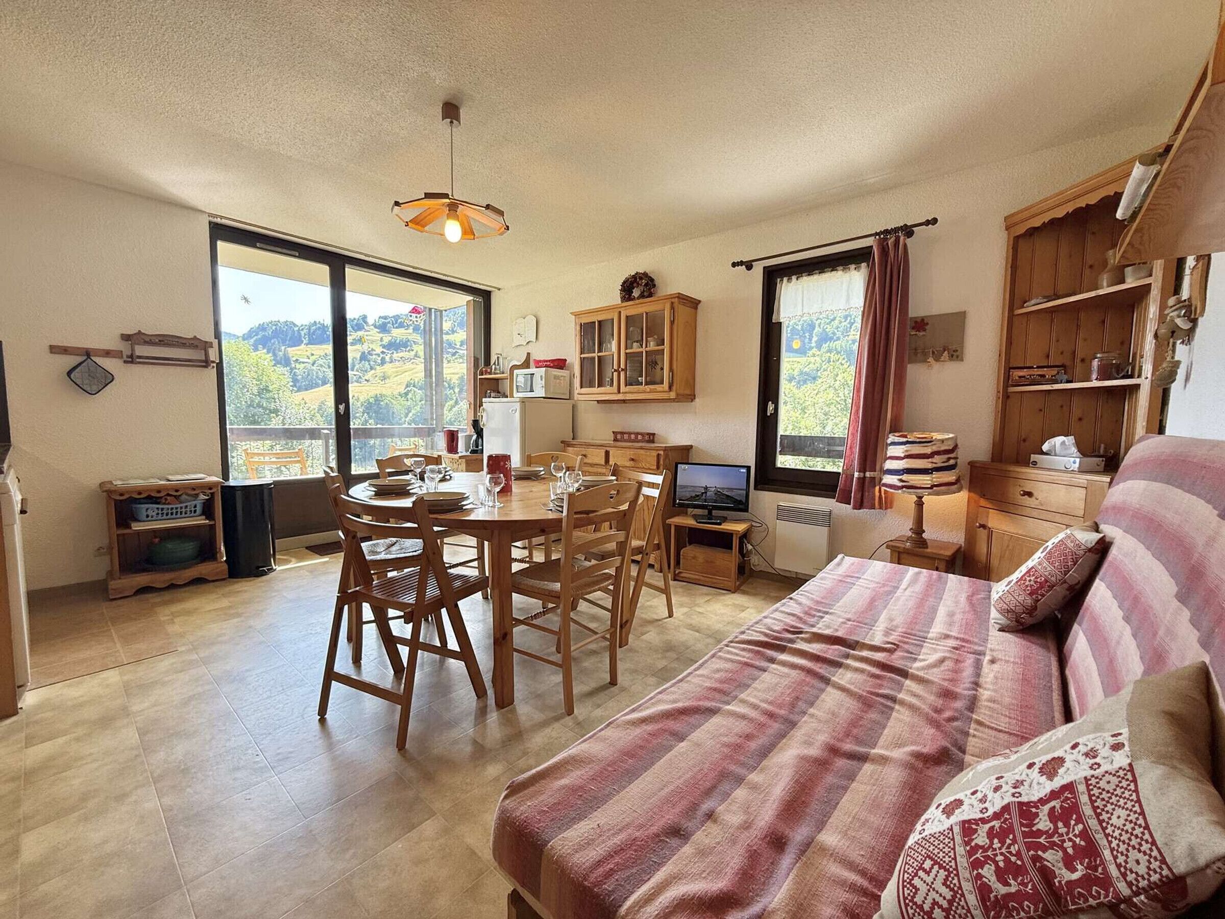 Ein gemütliches Zimmer mit einem Bett, einem Esstisch mit Stühlen, einem Fernseher und Blick ins Freie.