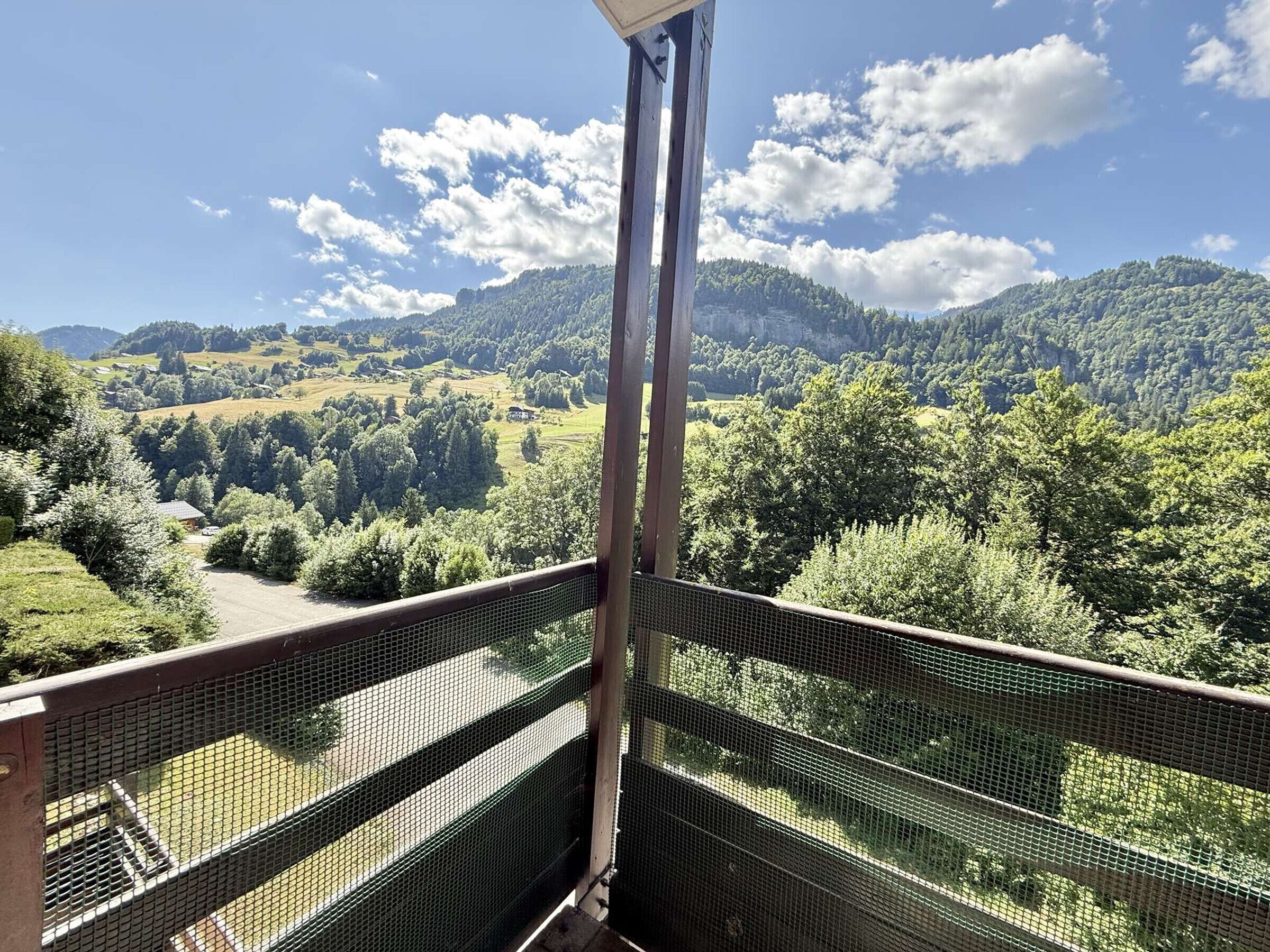 A balcony with a metal railing overlooking a scenic landscape with hills and trees.