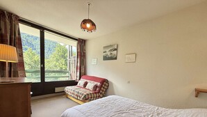 A bedroom with a large window, a bed, a chair, a desk, and a hanging light fixture. - 3-room apartment in Flumet - Parking - 6 people (Flumet)