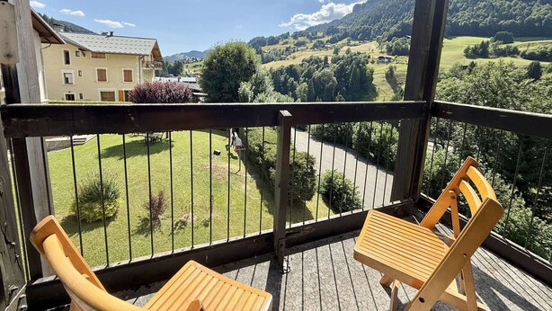 A balcony with two wooden chairs and a table, overlooking a green valley and a building with a yellow facade. - 3-room apartment in Flumet - Parking - 6 people (Flumet)