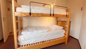 A bunk bed with two levels, a wooden headboard, and a bedside table with a lamp. - Cozy Apartment Near Slopes with Balconies (Montvalezan-La Rosière)