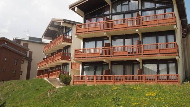 A multi-story hotel with balconies, a staircase leading to the entrance, and a grassy area in front. - Cozy Apartment Near Slopes with Balconies (Montvalezan-La Rosière)