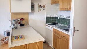 A compact kitchen with wooden cabinets, a white countertop, and a green-tiled backsplash. - Cozy Apartment Near Slopes with Balconies (Montvalezan-La Rosière)