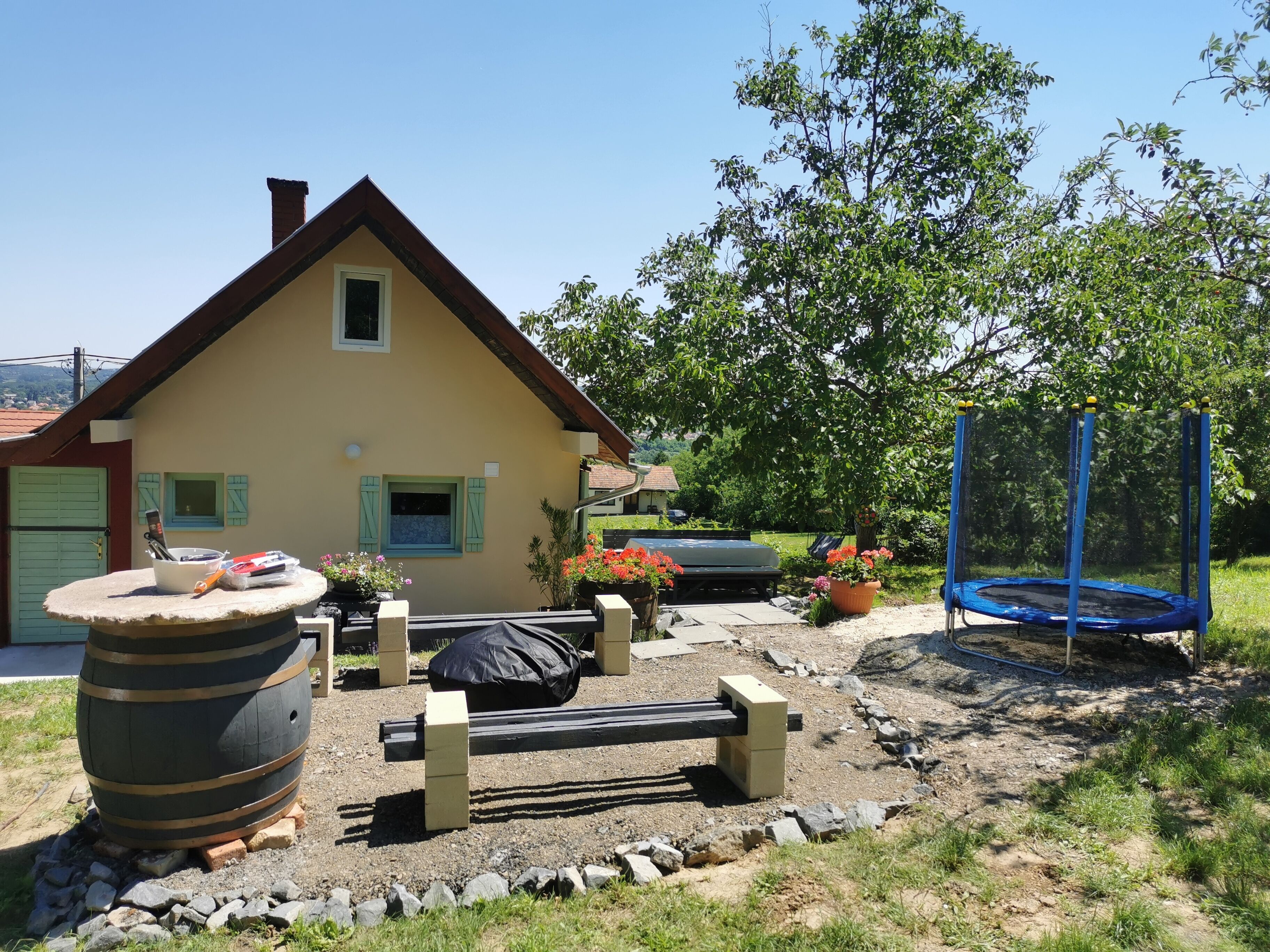Une maison avec un toit en pente, un porche à l’avant et un trampoline dans le jardin.