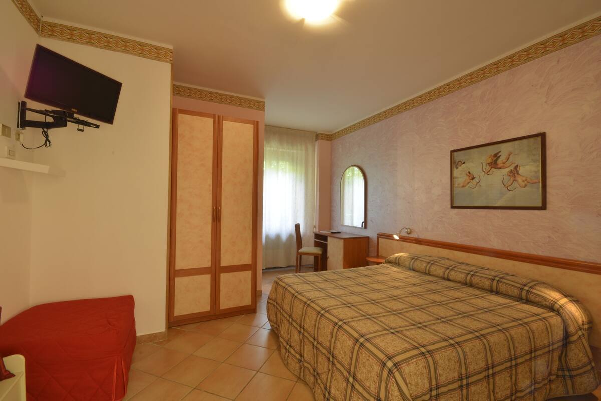 A bedroom with a bed, a desk, a chair, a television, and a wardrobe.
