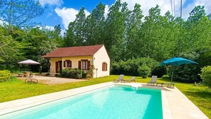 A rectangular swimming pool with a tiled deck, a small house with a red roof, and two sun loungers with umbrellas. - La Petite Fagette (Frayssinet-le-Gélat)