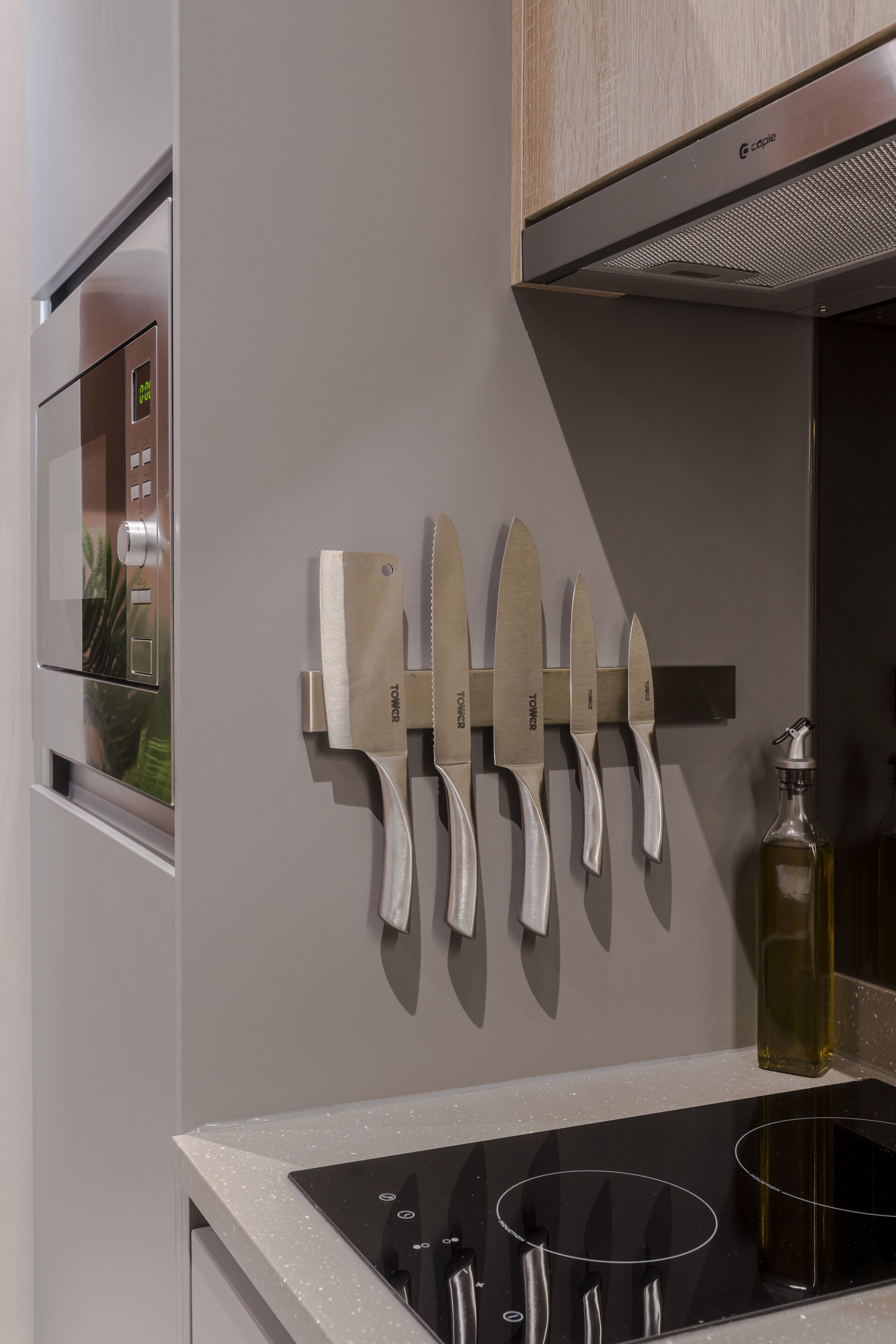 A modern kitchen with a built-in oven, a stovetop, and a knife rack on the wall.