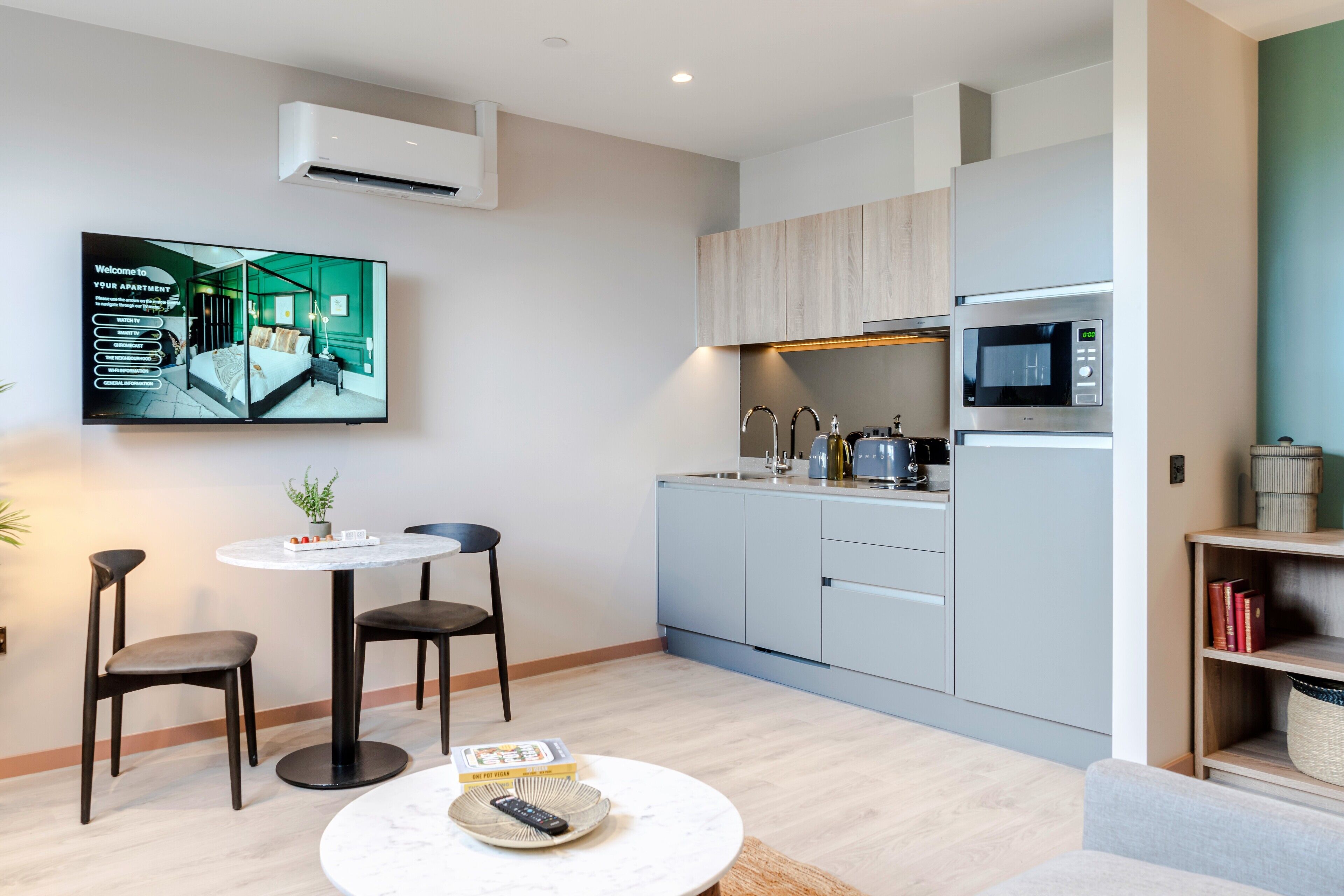 A modern apartment with a kitchen, dining area, and a flat-screen TV mounted on the wall.