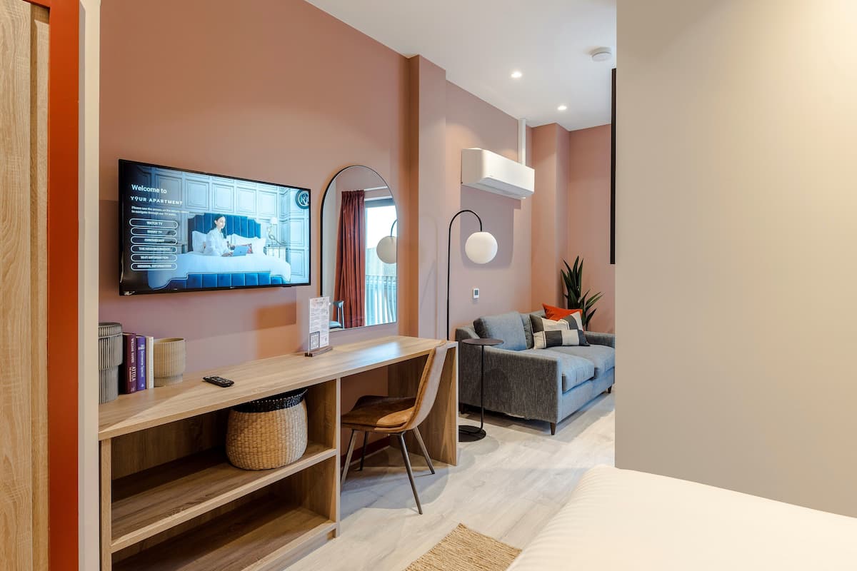 Un salon moderne avec un bureau en bois, un canapé gris et un téléviseur à écran plat fixé au mur.