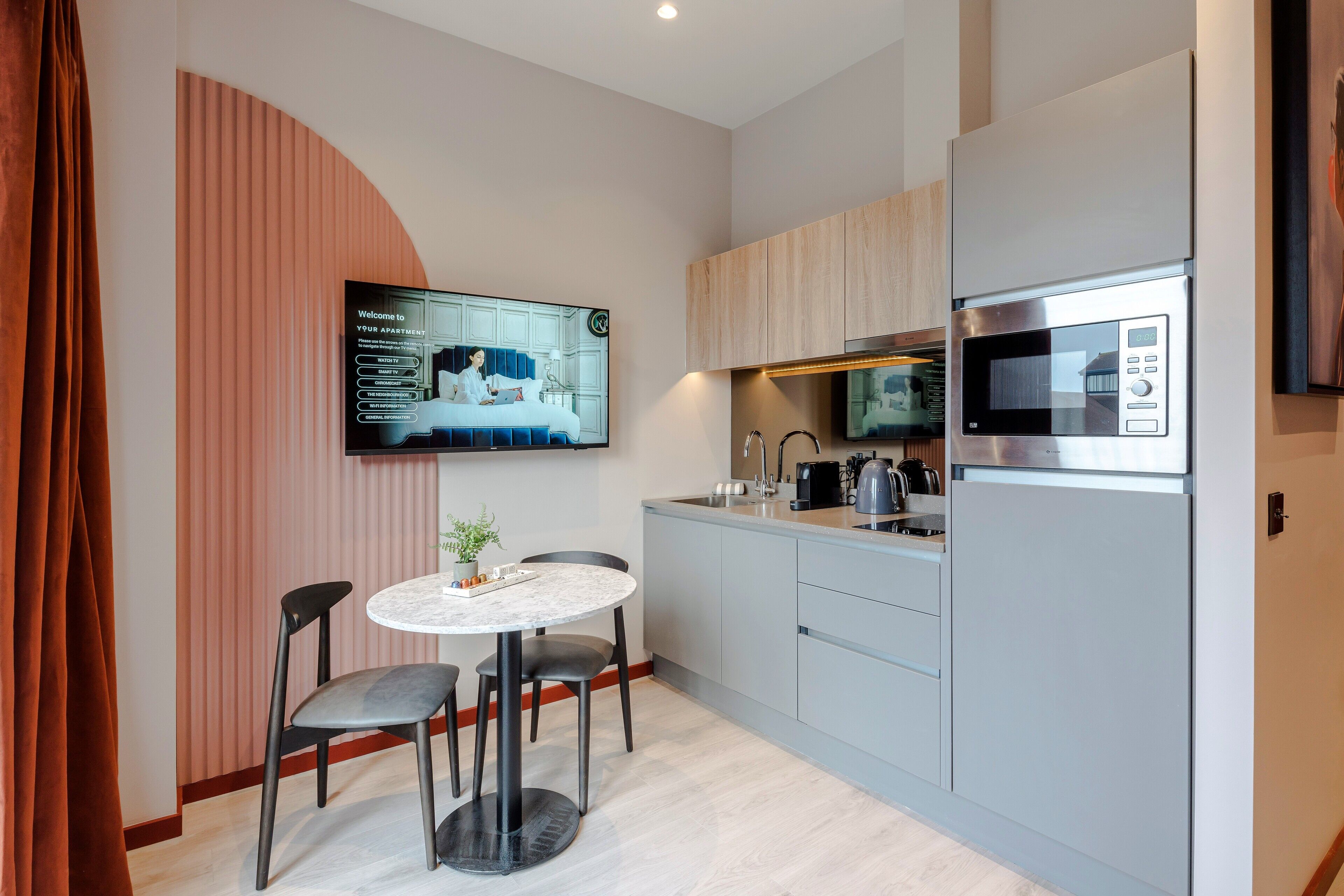 Een moderne keuken met een ingebouwde magnetron, een eethoek met een ronde tafel en stoelen, en een flatscreen-televisie aan de muur bevestigd.