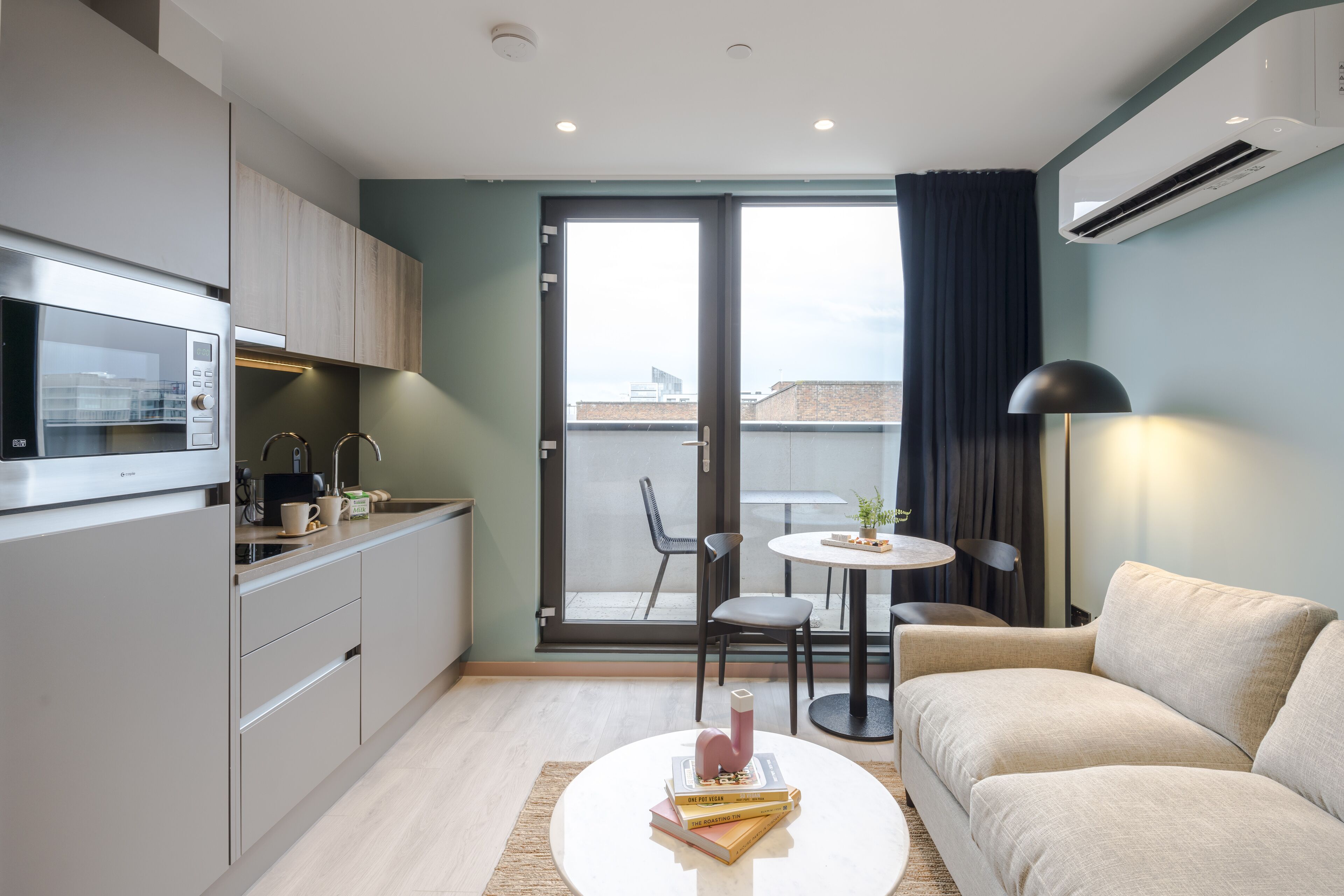 Un apartamento moderno con kitchenette, zona de comedor, sofá y vistas a través de un gran ventanal corredero.