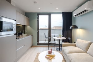 Un apartamento moderno con kitchenette, zona de comedor, sofá y vistas a través de un gran ventanal corredero.