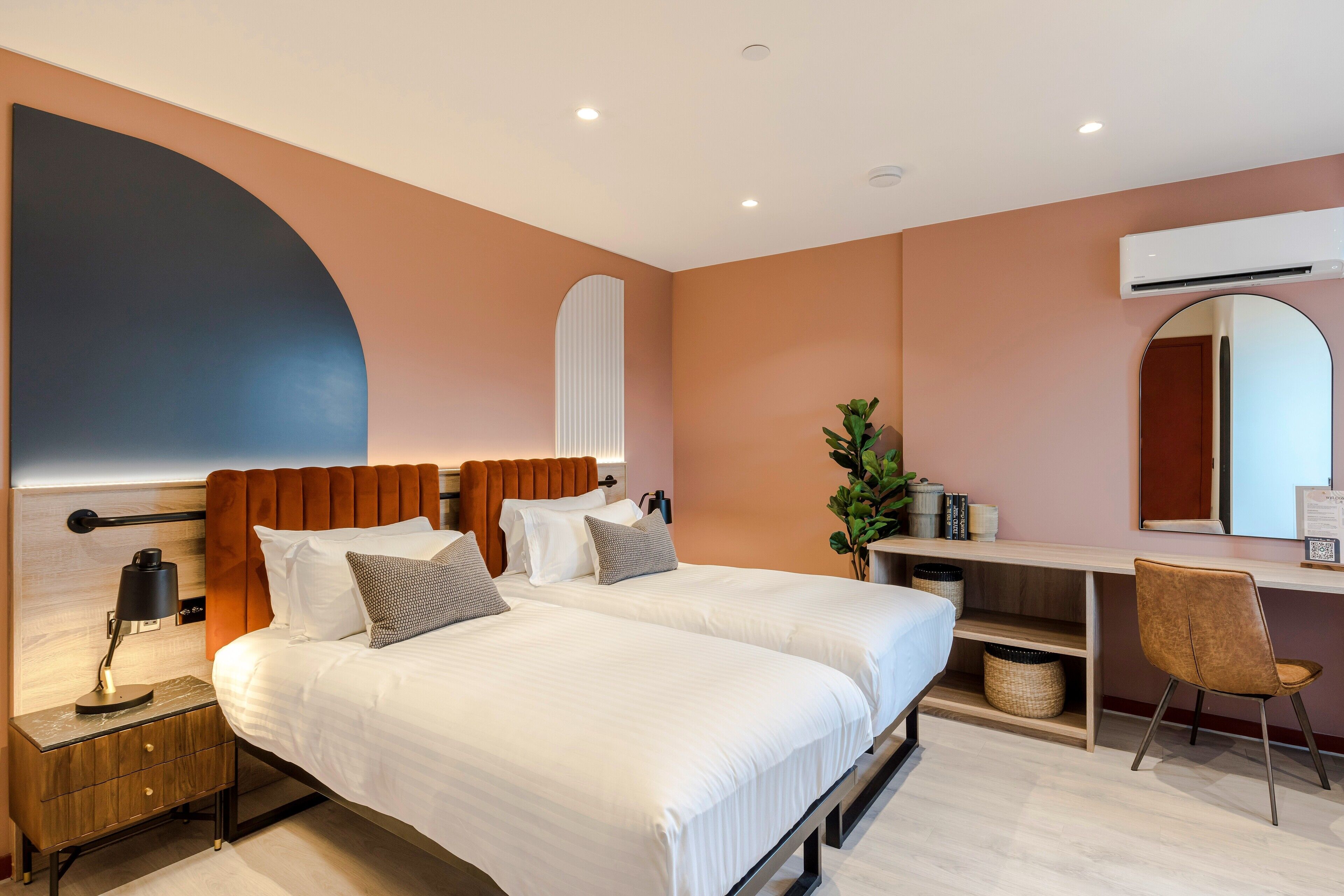 Una habitación de hotel moderna con dos camas, un escritorio, una silla y un espejo grande.