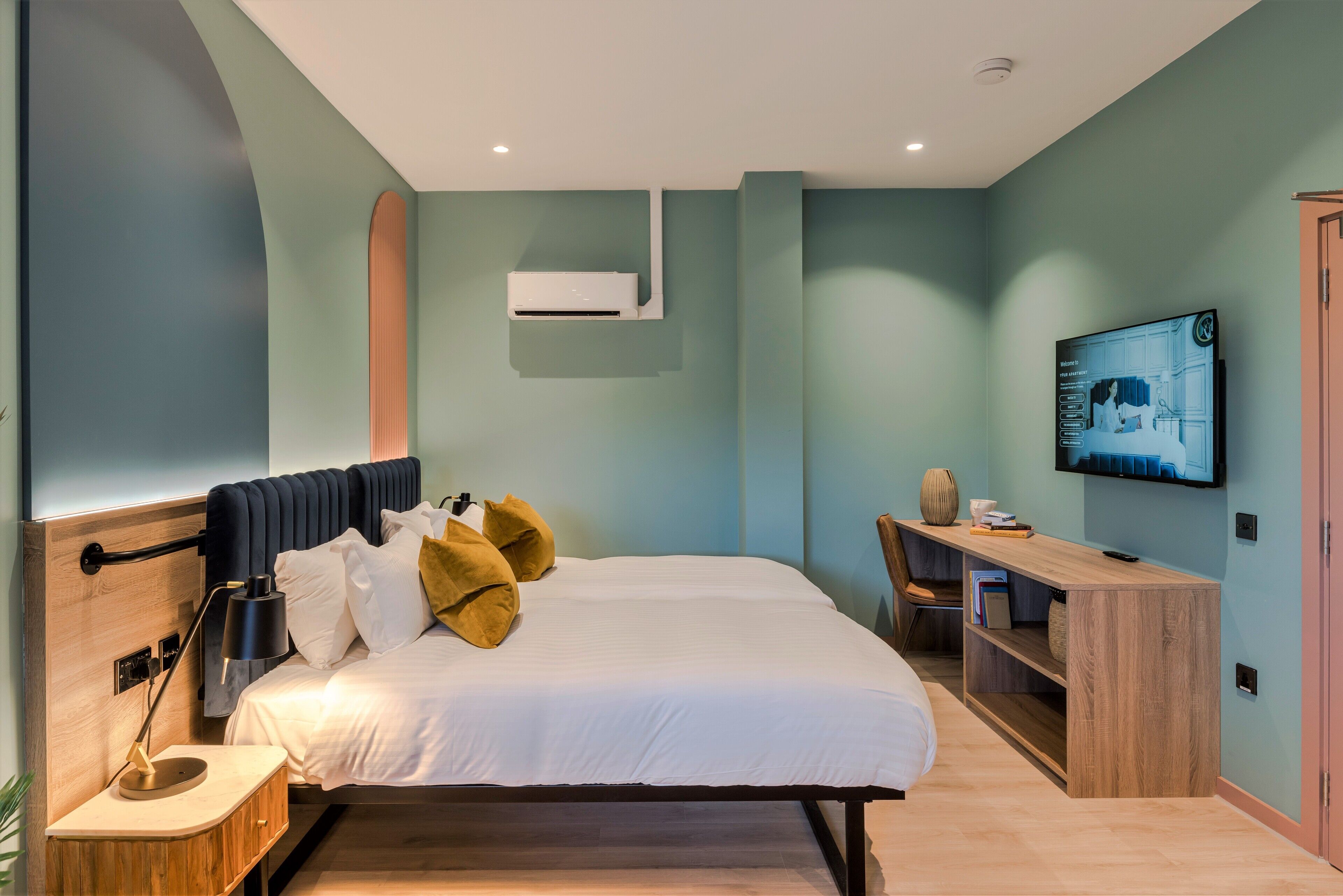 Ein modernes Schlafzimmer mit Bett, Nachttisch, Fernseher und Schreibtisch mit Stuhl.