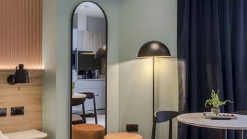 Ein modernes Hotelzimmer mit einer Wand in Holzoptik, einem runden Tisch mit einem Topfpflanzen und einem Spiegel, der den Küchenbereich reflektiert.