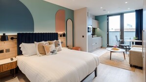 A modern hotel room with a large bed, a desk, and a dining area.