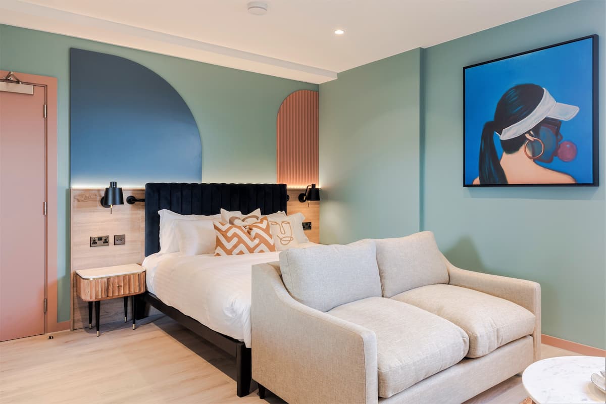 Une chambre à coucher moderne avec un lit, un canapé, une table de chevet et un tableau au mur.