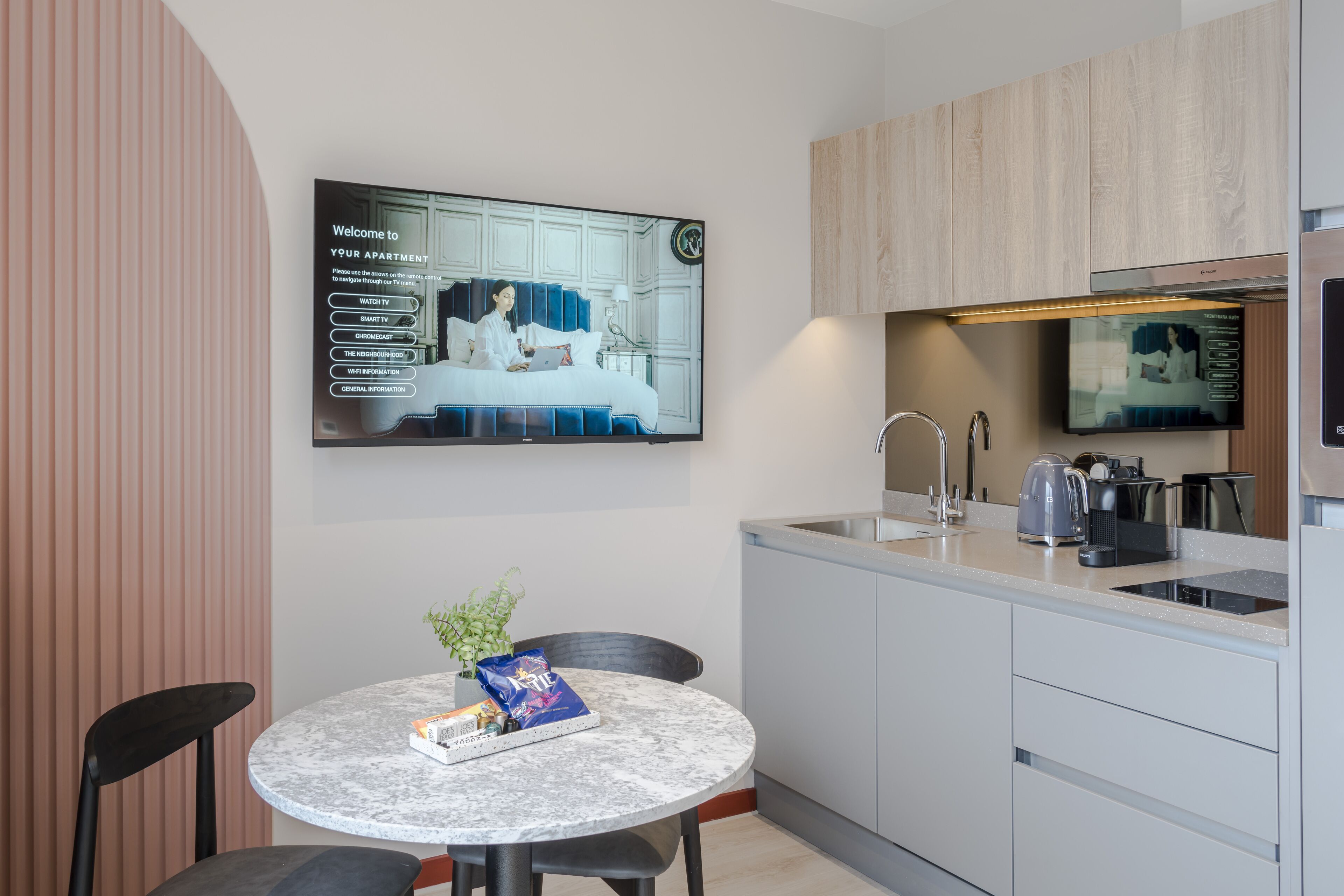 Una cucina moderna con TV integrata, un'area pranzo con tavolo e sedie, e una piccola pianta sul tavolo.