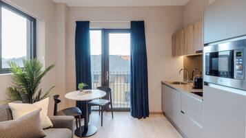 A compact kitchen with a dining area, a sofa, and a large window with curtains.