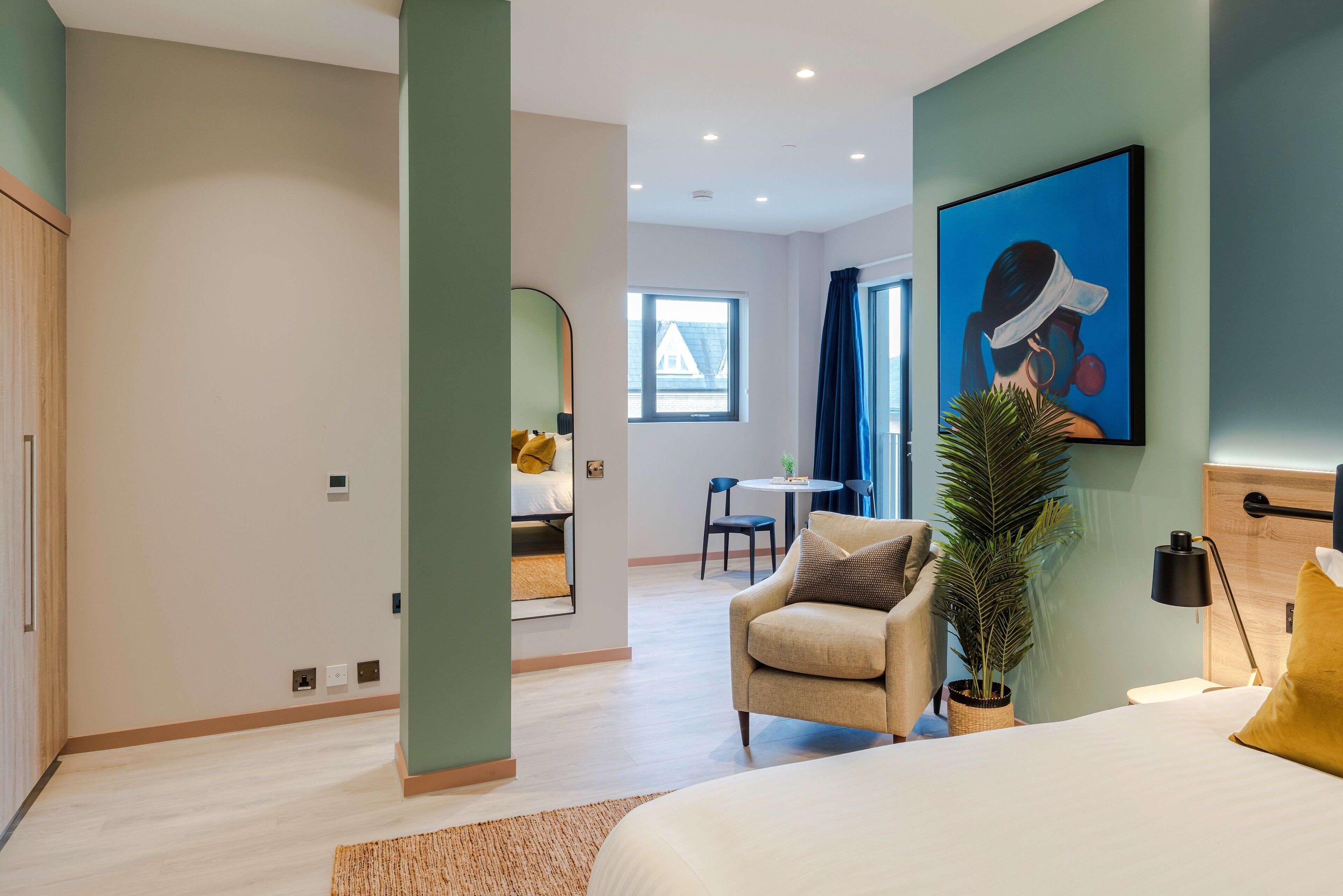 A modern hotel room with a bed, a sofa, a desk, and a large window.