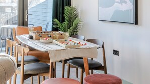 A dining area with a table set for two, a potted plant, and a framed artwork on the wall.