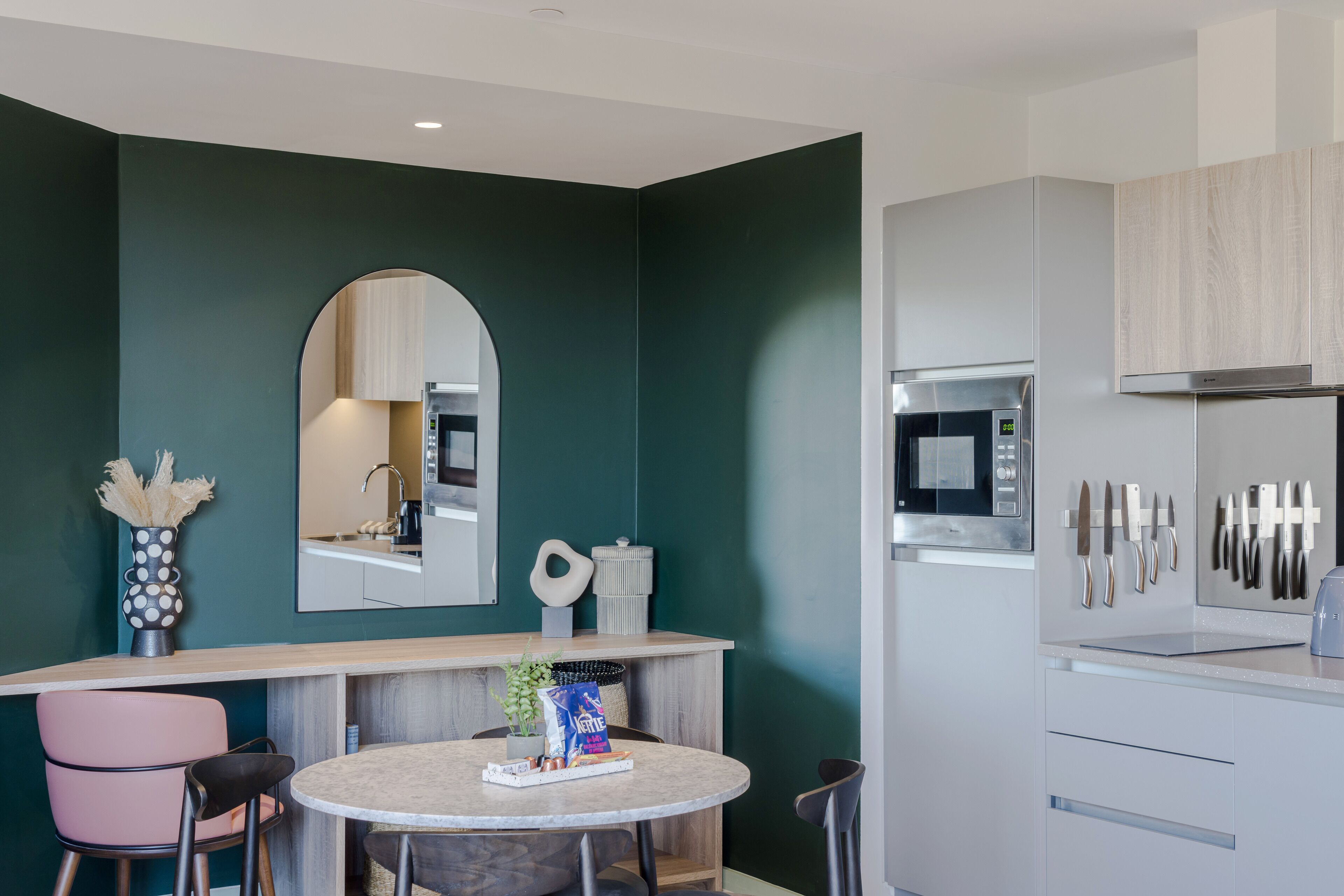 A modern kitchen with a microwave, knife rack, and a round dining table with chairs.