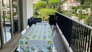 Un balcó amb una taula preparada per dinar, envoltat de cadires i una barana.
