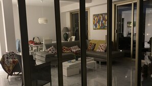 Un saló modern amb un sofà, butaques i una taula de centre. Es veu una zona de menjador amb una taula i caires a través d'una porta de vidre.