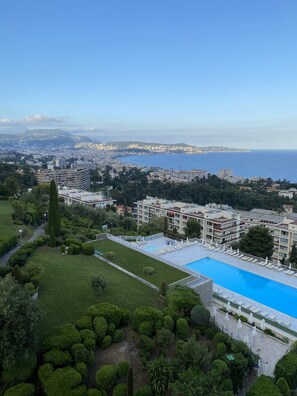 A hotel with a swimming pool, surrounded by well-maintained gardens and a view of the sea.