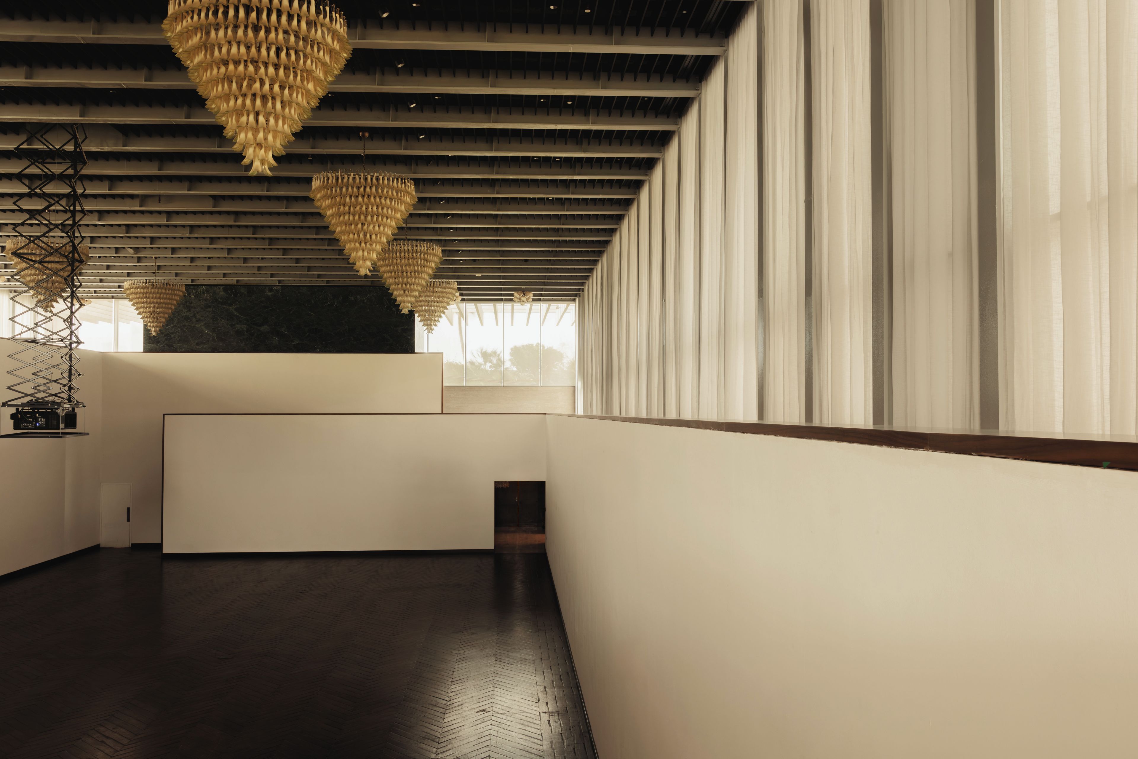 A spacious interior with high ceilings, modern chandeliers, and a long corridor with a wooden floor.