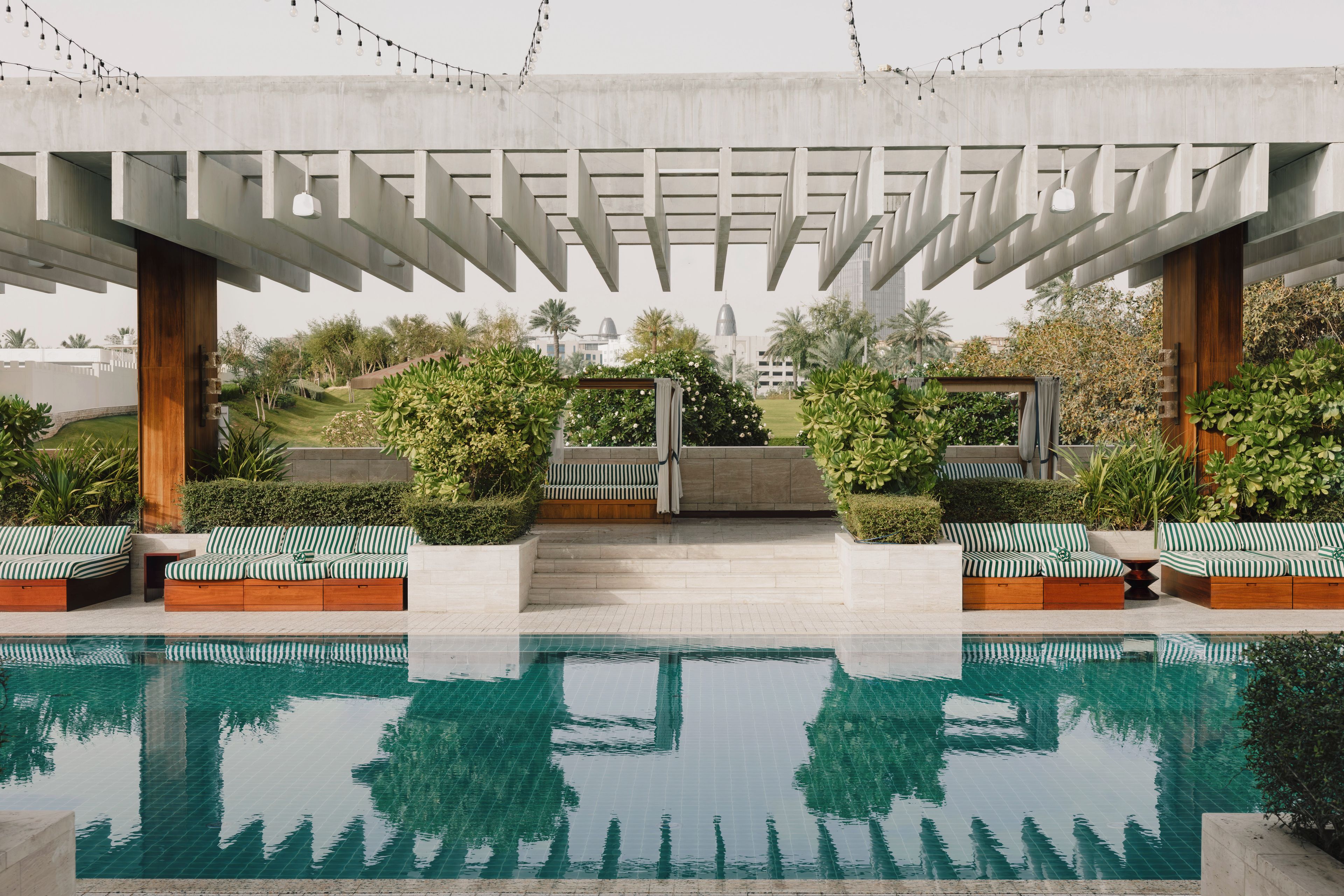 A pool area with a clear view of the city skyline, outdoor seating with striped cushions, and a pergola structure.