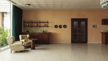 A spacious room with a large window, a seating area with a chair and a small table, a wooden cabinet with decorative items, and a door with a frosted glass panel.