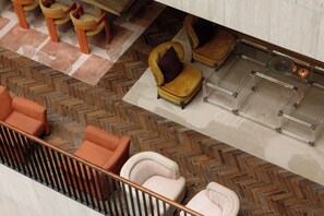 A modern interior with a herringbone floor pattern, a glass coffee table, and a seating area with orange and white chairs. - The Ned Doha (Doha)