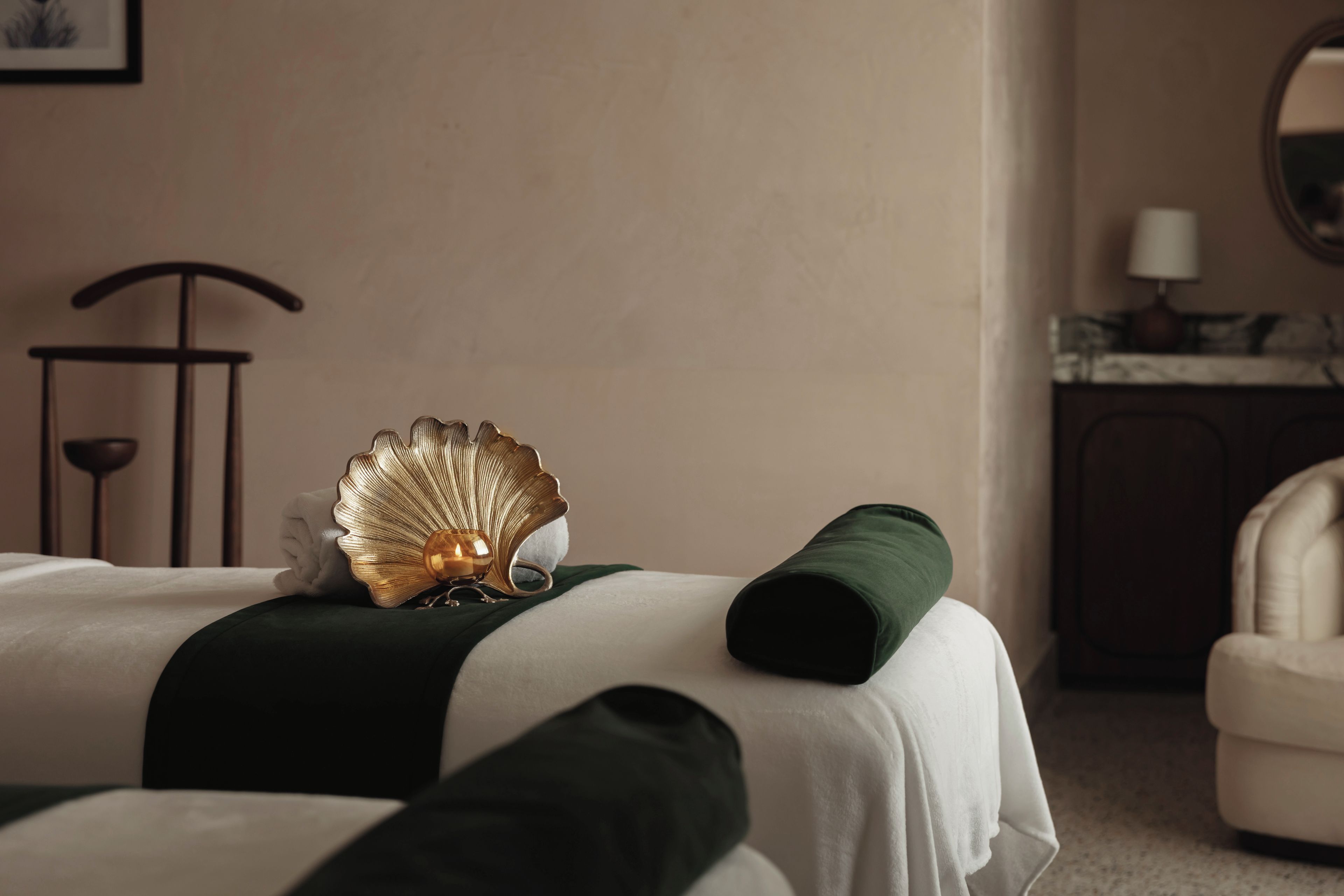 Quarto de hotel com uma cama, um travesseiro verde, uma concha decorativa e uma mesa de cabeceira com abajur.