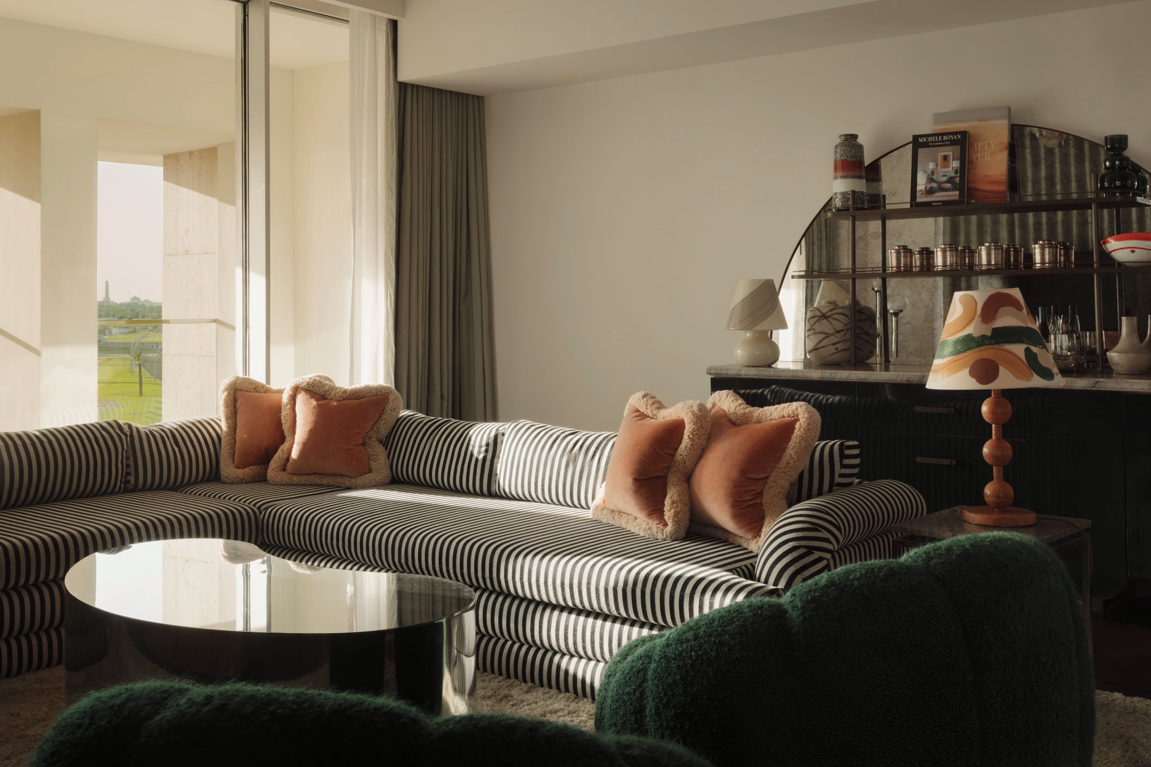 Een moderne woonkamer met een gestreepte bank, een ronde salontafel en een dressoir met planken.